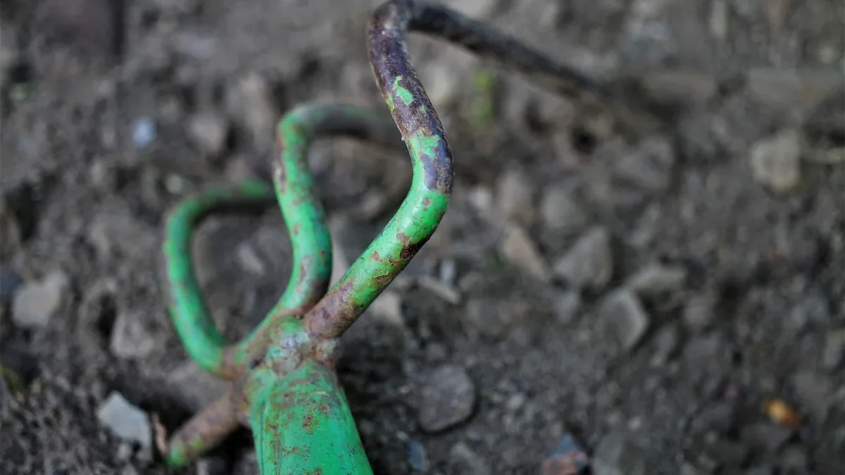 A green metal tool with a curved handle and a flat, rectangular head, lying on the ground.